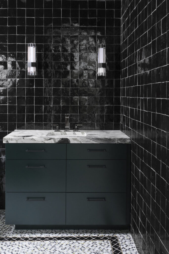 Bathroom setting with black glossy tiles on the wall, dark vanity, and penny tile on the floor.